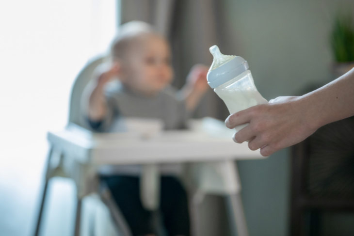 Baby sitting in a high chair, waiting for a bottle.